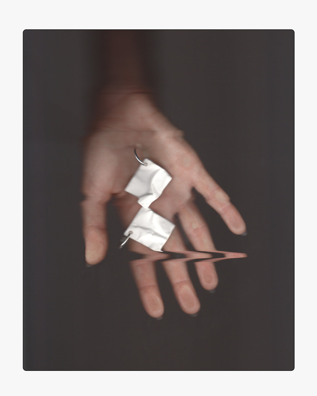 Minimalist hand holding a hand-cast white ceramic crinkle earring on sterling silver hoops, featuring a subtle reflection.