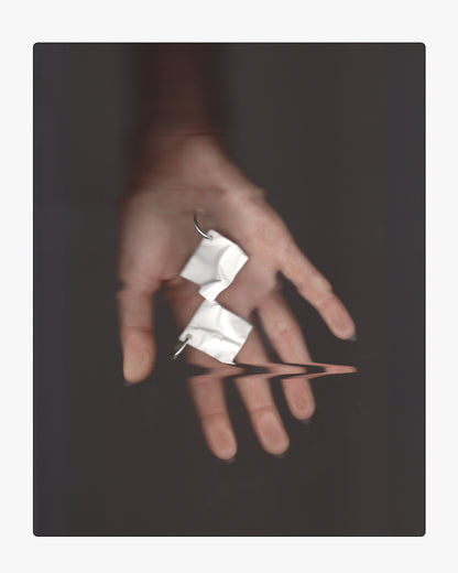 Minimalist hand holding a hand-cast white ceramic crinkle earring on sterling silver hoops, featuring a subtle reflection.