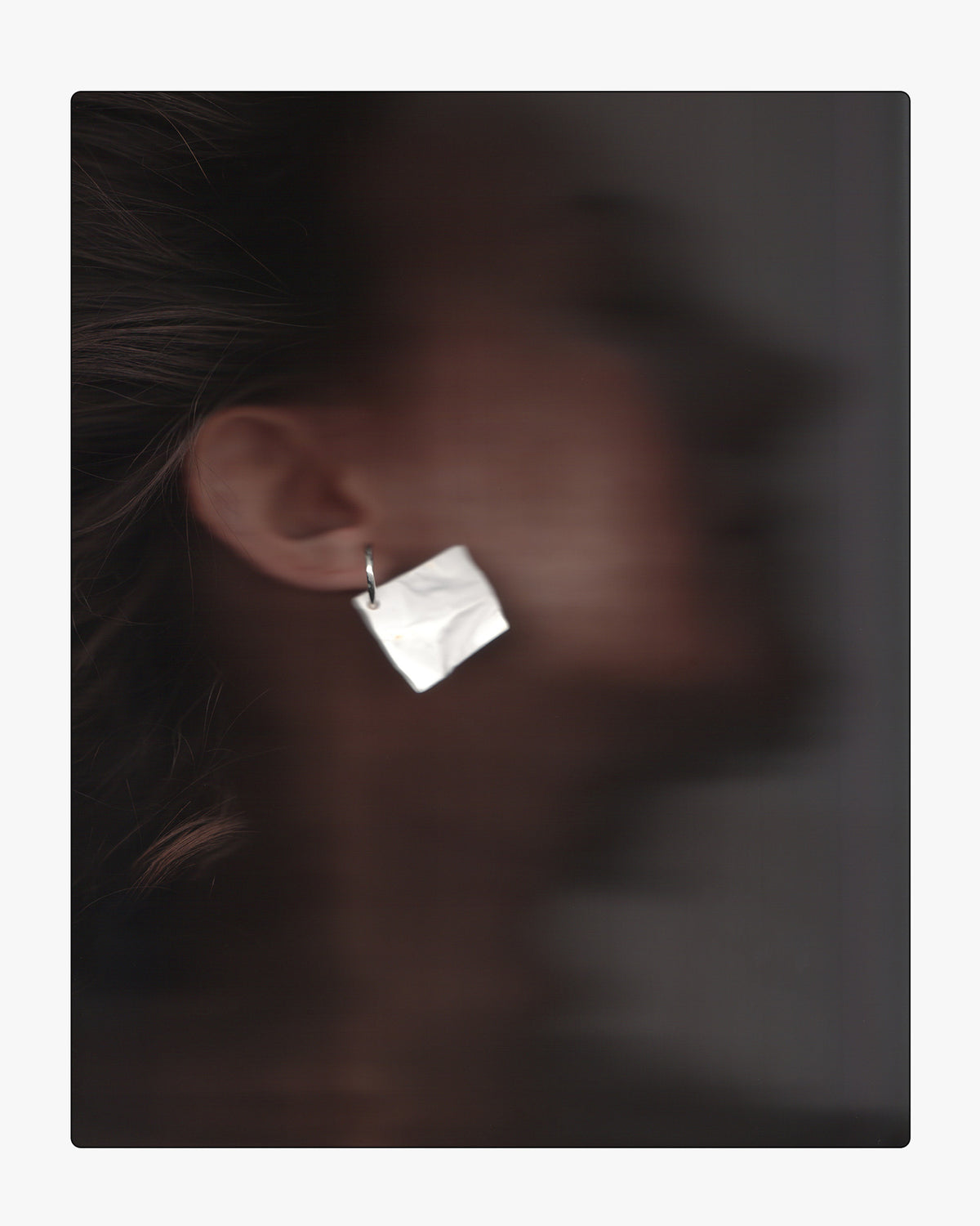 Model wearing a modern, hand-cast white ceramic crinkle-texture drop earring on a sterling silver hoop, showing scale and placement on the ear.