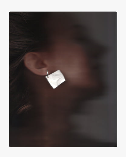 Model wearing a modern, hand-cast white ceramic crinkle-texture drop earring on a sterling silver hoop, showing scale and placement on the ear.