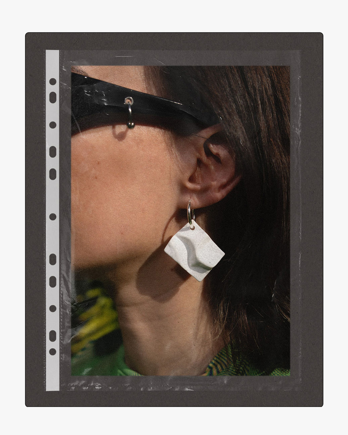Model wearing a hand-cast white ceramic drop earring, shown inside a black film sleeve frame.