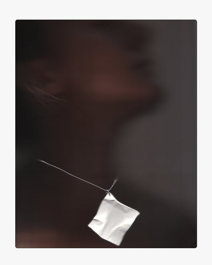 Mood-lit close-up of the white ceramic paper-texture Draft 01 necklace pendant against subtle shadow.