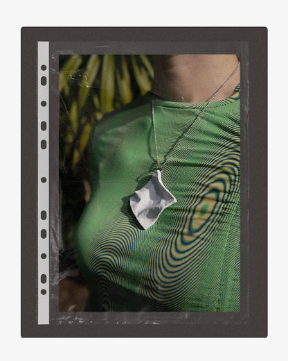 Model wearing a white ceramic pendant necklace, presented in a film sleeve frame.