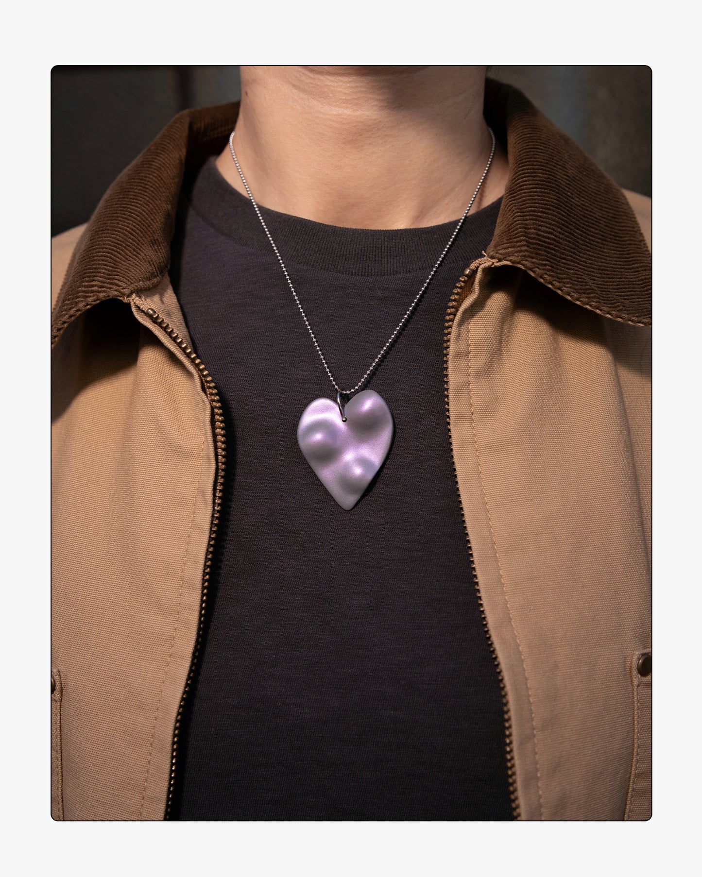 A model wearing the TOPO Heart in Nebula; a sculptural ceramic heart necklace that shifts from grey to violet in the light, representing an internal dimension.
