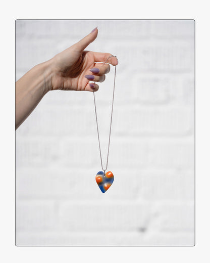 Hand holding a the Topo heart necklace, showing the 18" silver ball chain against a white background.