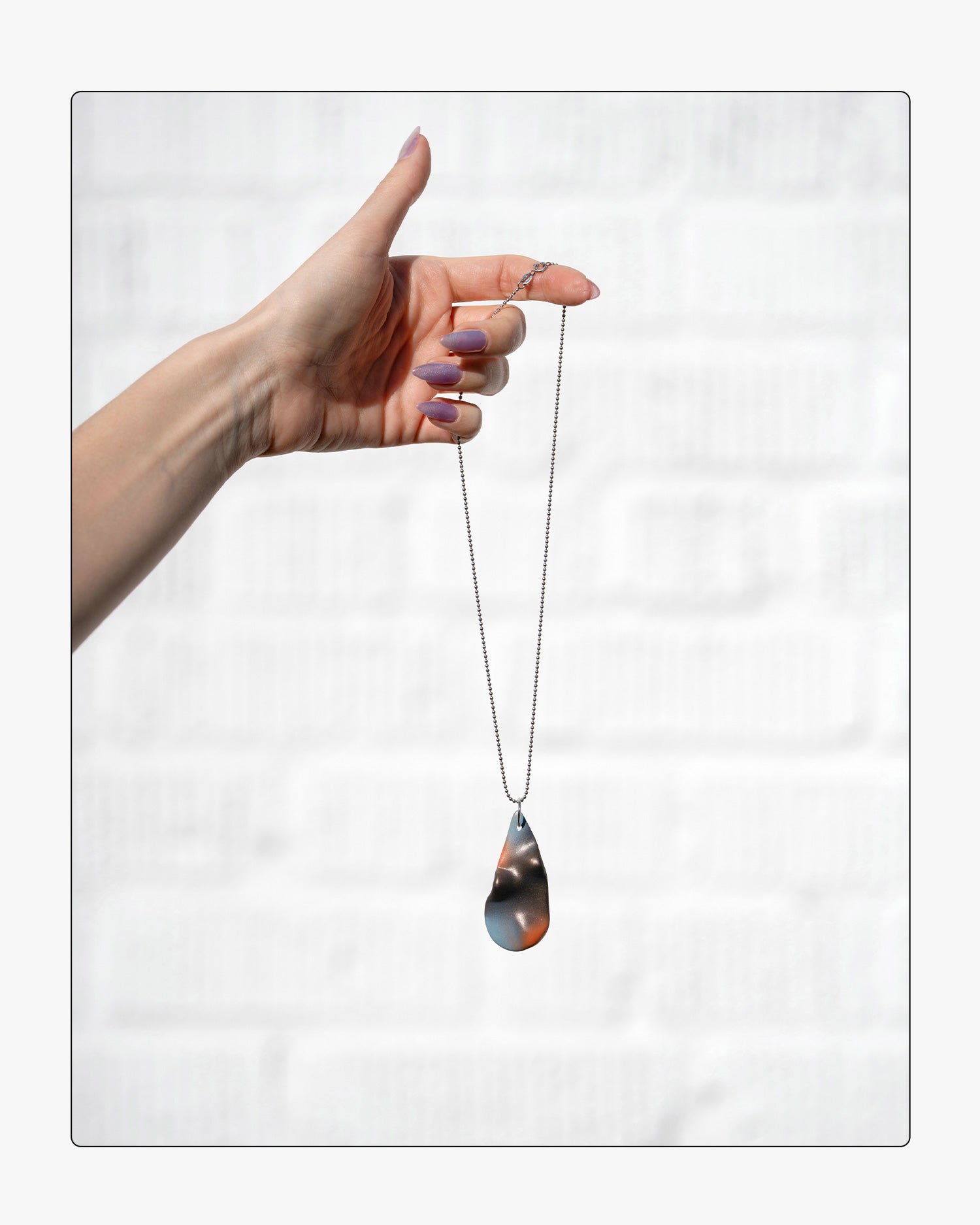 Hand holding a teardrop-shaped airbrushed ceramic pendant on a white background