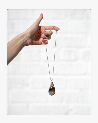 Hand holding a teardrop-shaped airbrushed ceramic pendant on a white background