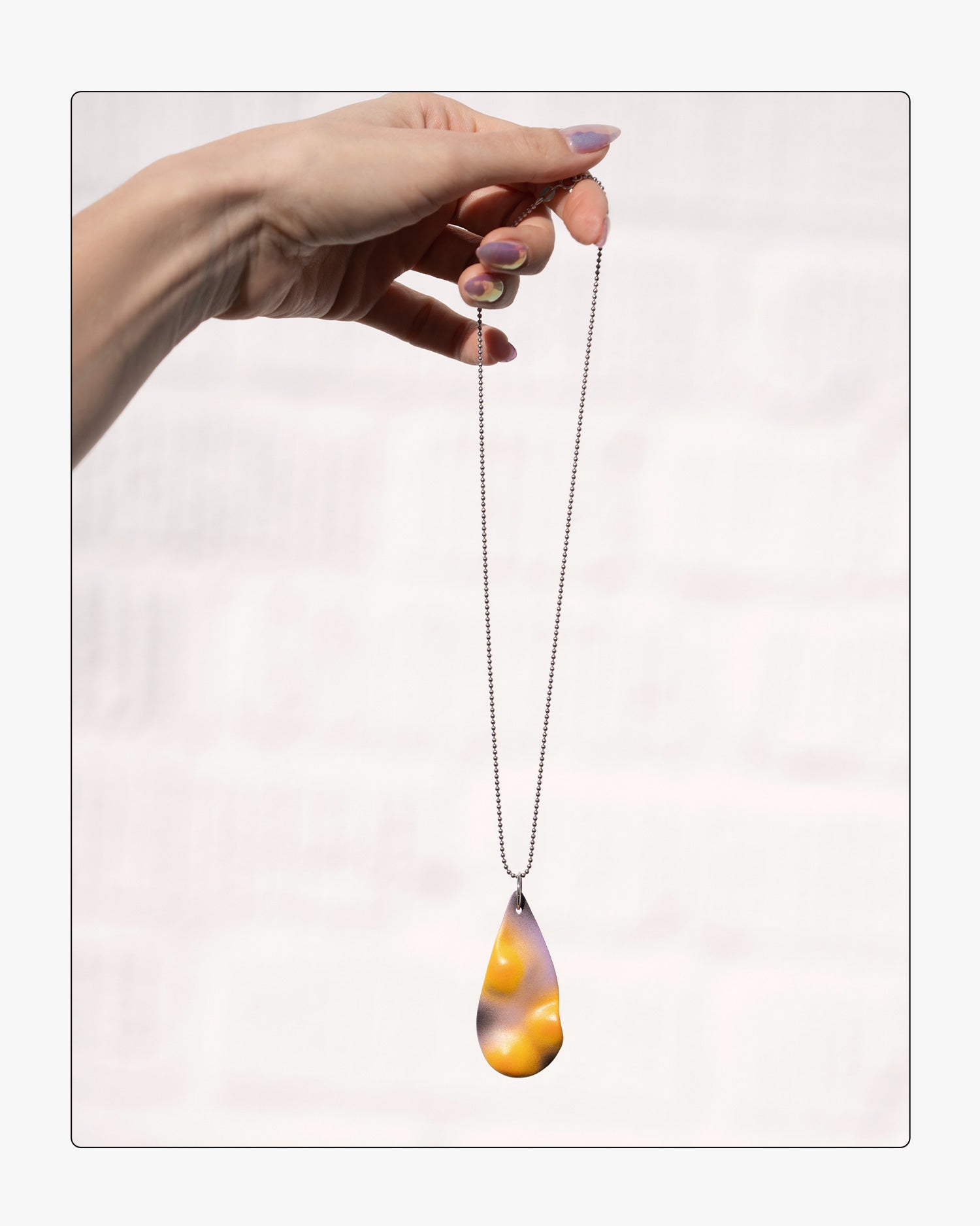 A hand holding the Eclipse ceramic pendant against a white background, revealing the tactile topographic ridges and the soft gradient transition from pale pink to deep black.