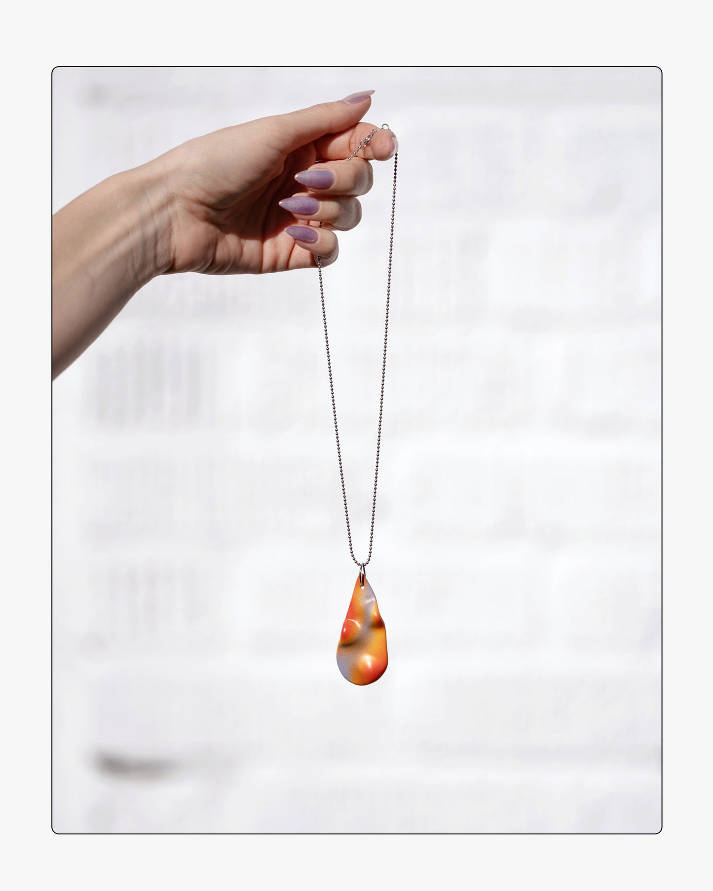 Handheld view of the TOPO Teardrop in Frequency, highlighting the unique, hand-painted details and organic shape of the ceramic pendant against a white background.